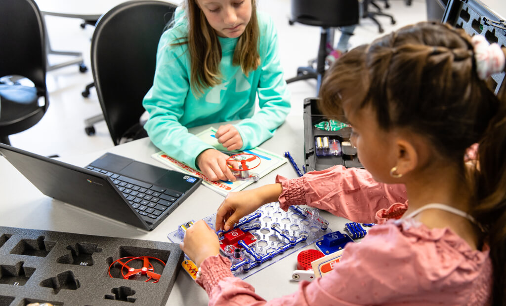 two students work together on building STEM-related projects at a lab table in a school setting